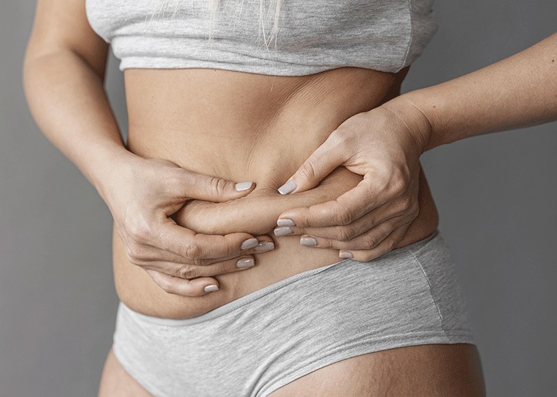 Close-up of a woman pinching abdominal fat, illustrating areas commonly treated in liposculpture to achieve a more contoured shape